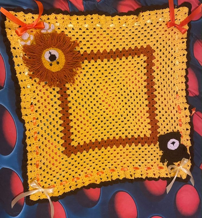 Little Lion Blanket: A golden granny-square baby blanket with a crocheted lion and ribbon ties.